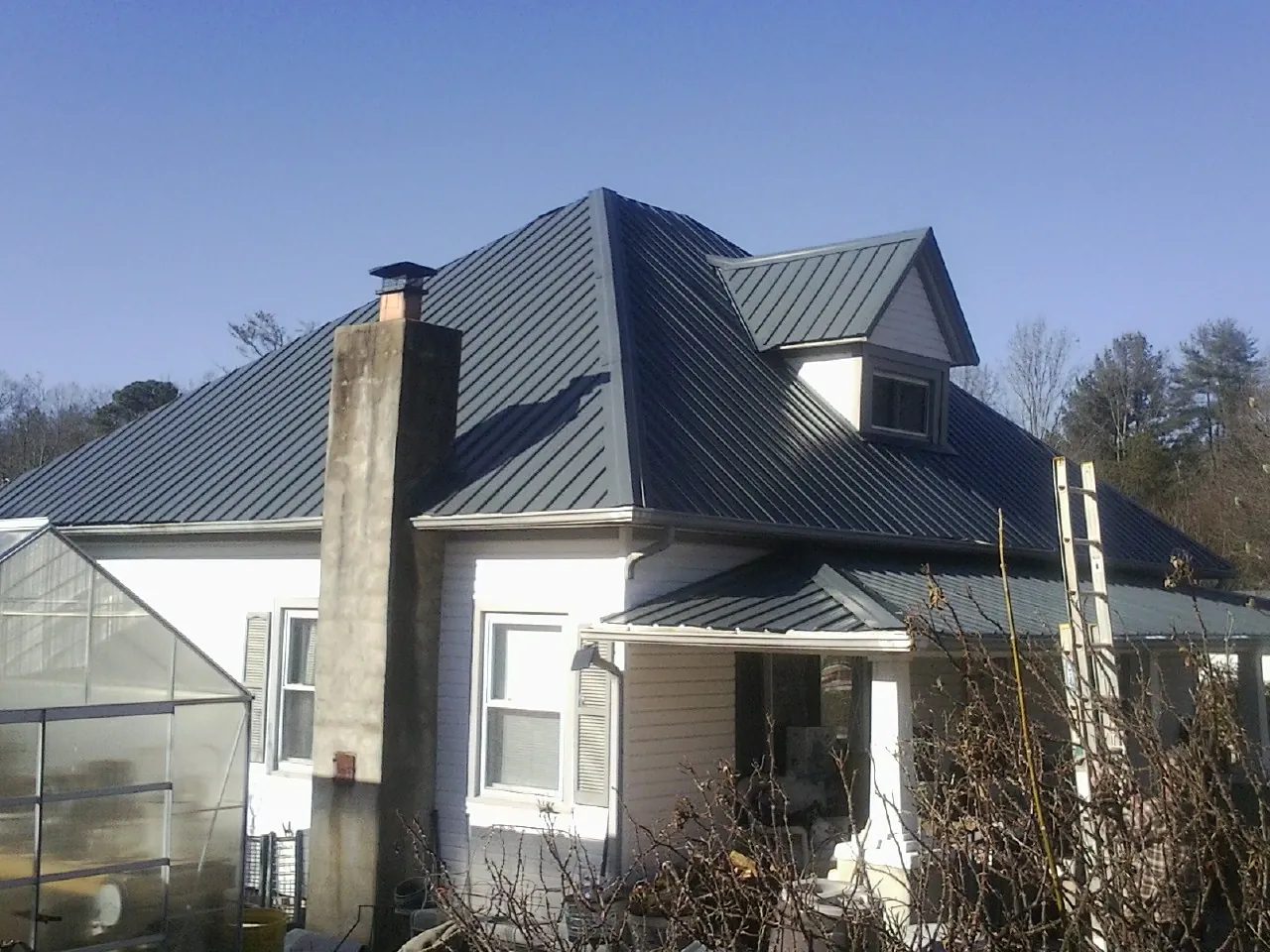 Dark blue standing seam metal roof on a white farmhouse with dormer — Slate & Tile Roof Repair by Roofing Brothers in Palm Harbor