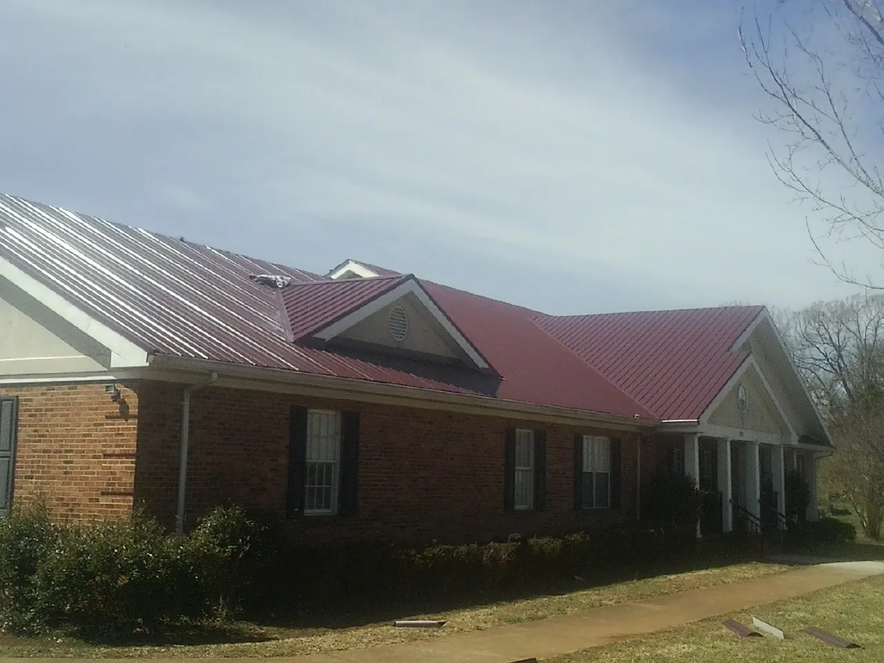 Red metal roof with gabled entries on a long brick building, from a Hail Damage Roof Repair job in Palm Harbor