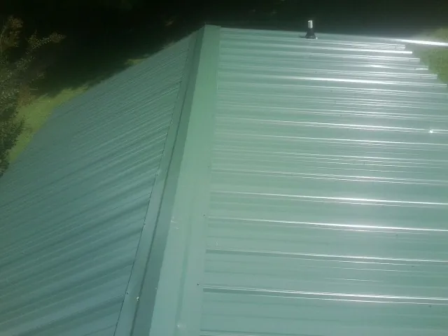New green metal panels meeting at the ridge of a roof — Flat Roof Repair work by our crew in Palm Harbor