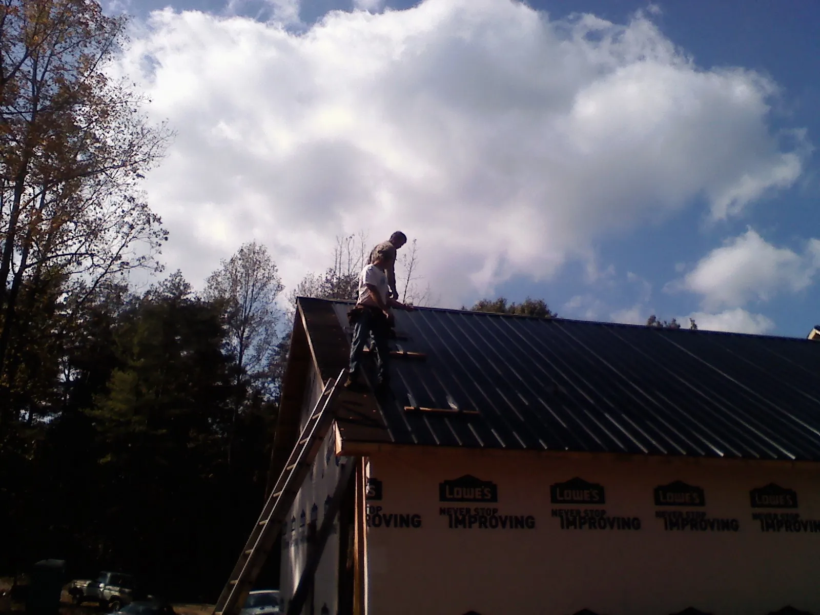Roofer fastening dark metal panels high against a cloudy sky, from a Roof Inspection job in Palm Harbor