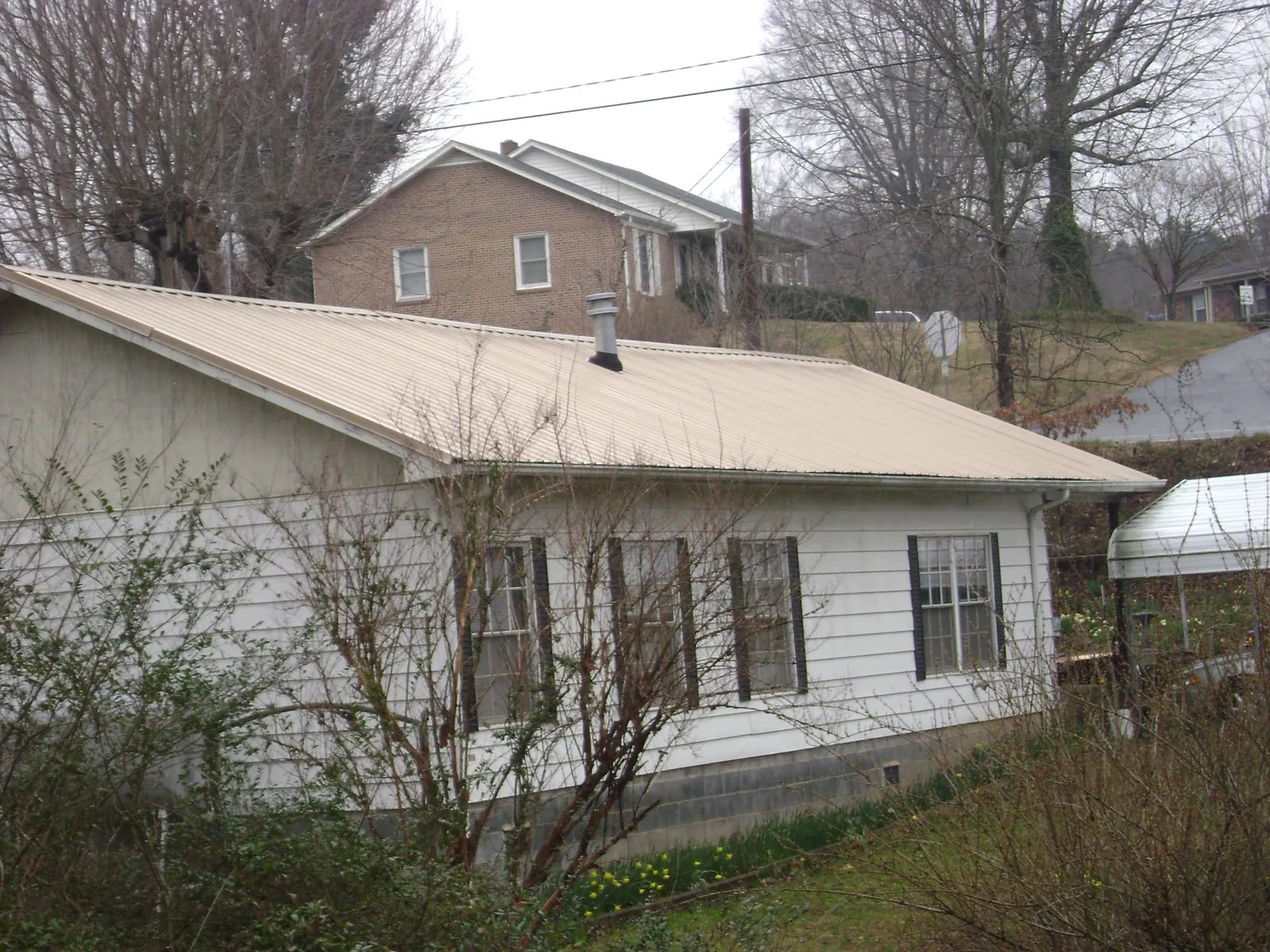 Tan metal roof on a white sided house set into a hillside — Commercial Roofing by Roofing Brothers in Palm Harbor